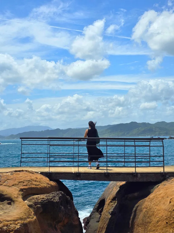 Femme admirant l’océan depuis une passerelle face aux montagnes