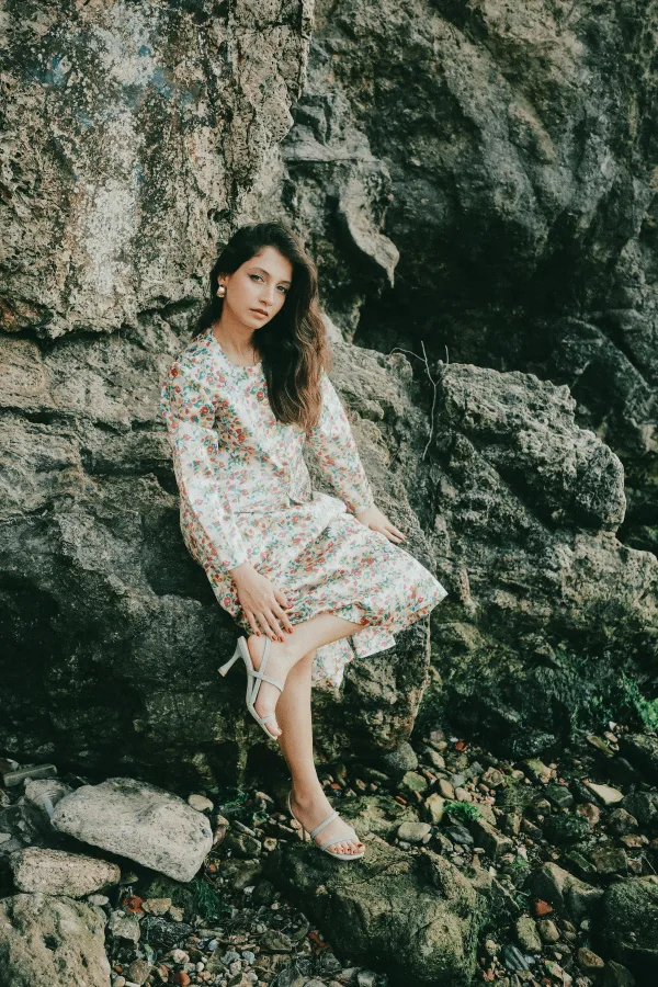 Jeune femme en robe fleurie assise sur des rochers