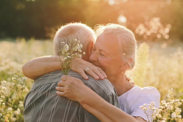 Couple de seniors s'enlaçant dans un champ de fleurs au coucher du soleil