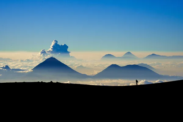 Silhouette d'un randonneur face aux volcans au-dessus des nuages