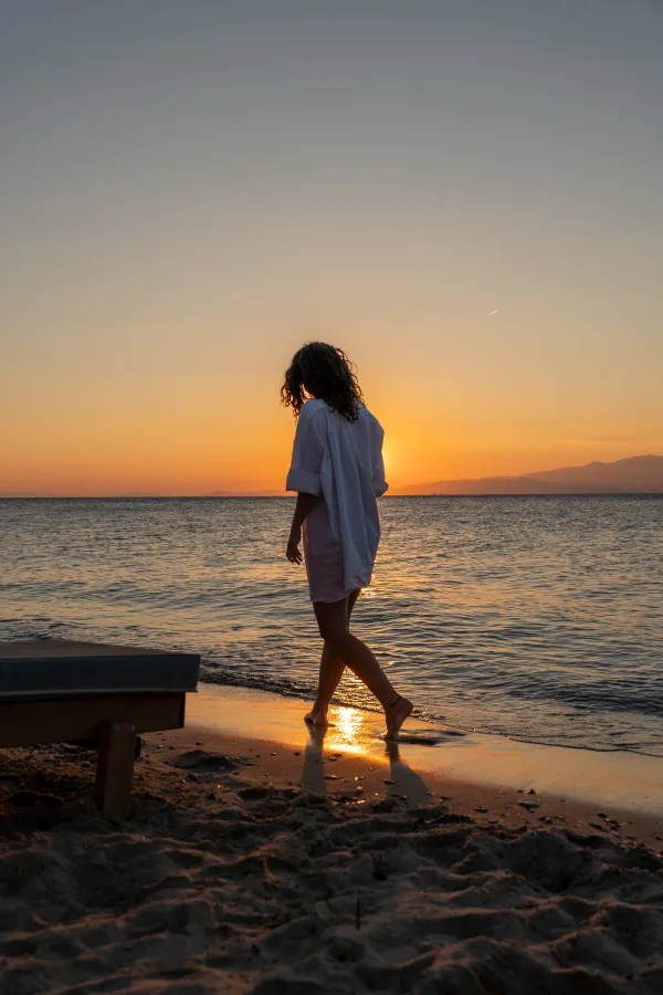 Silhouette d'une femme marchant sur la plage au coucher du soleil
