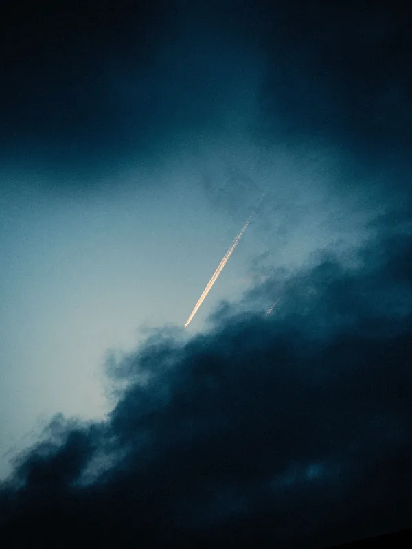 Traînée lumineuse d’un avion dans un ciel nuageux au crépuscule