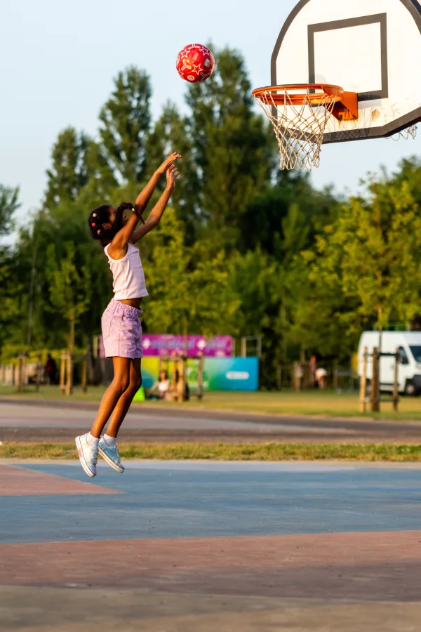 Jeune fille jouant au basketball sur un terrain extérieur au coucher du soleil