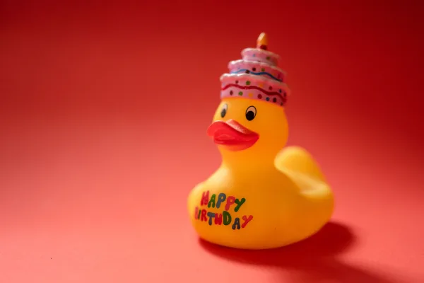 Canard jaune Happy Birthday avec chapeau d’anniversaire sur fond rouge