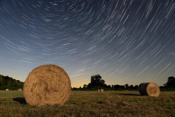Filé d’étoiles au-dessus d’un champ de ballots de foin sous un ciel nocturne