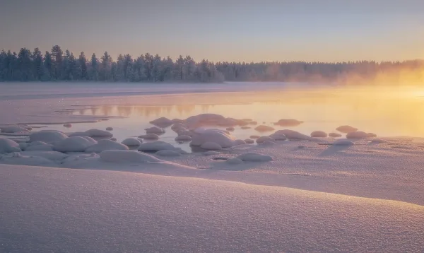 Lac enneigé au lever du soleil avec brume hivernale