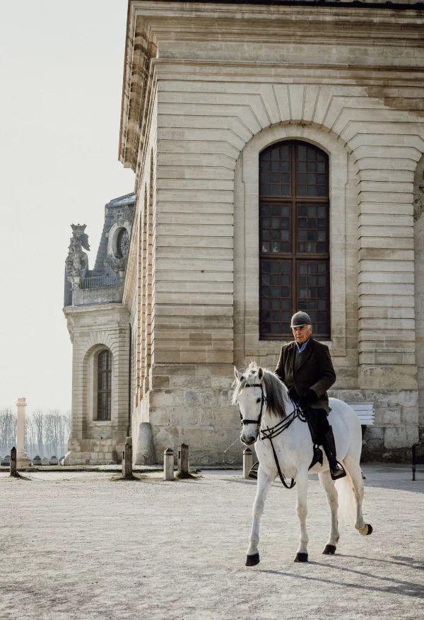 Cavalier sur cheval blanc devant un bâtiment historique majestueux