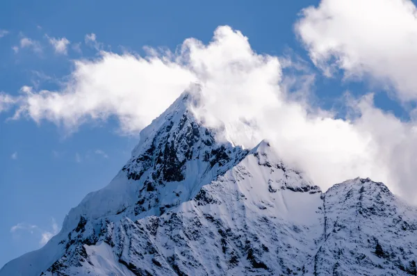 Sommet enneigé entouré de nuages sous un ciel bleu en haute montagne