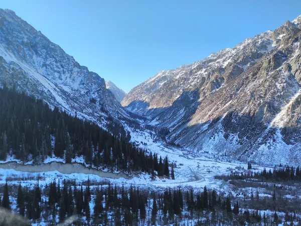 Vallée de montagne enneigée entourée de sommets rocheux sous un ciel bleu