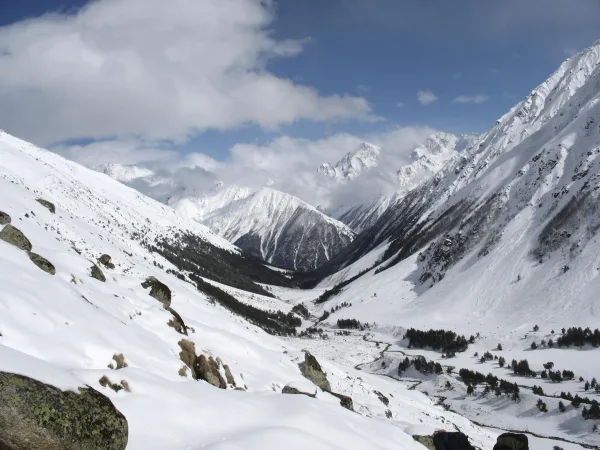 Vallée enneigée entourée de sommets majestueux sous un ciel nuageux