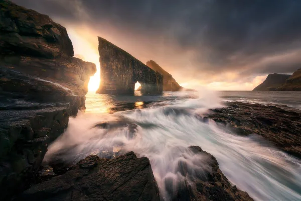 Vagues déchaînées frappant une arche rocheuse au coucher du soleil