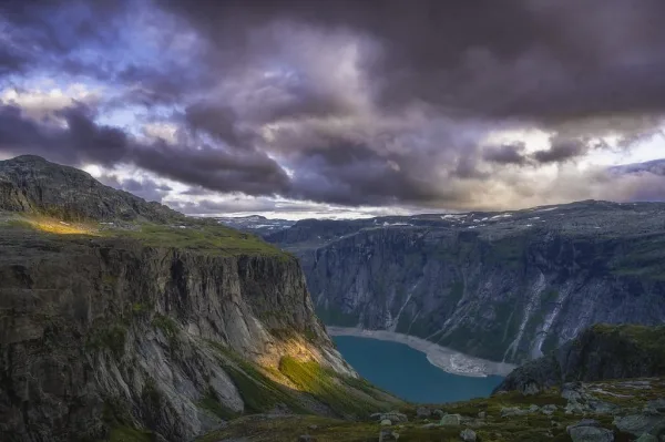 Falaises majestueuses dominant un lac de montagne sous un ciel orageux