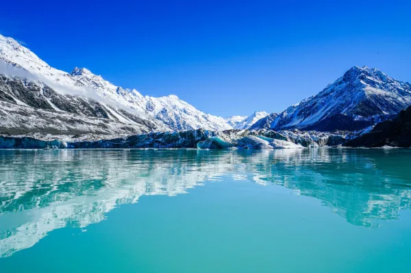 Lac glaciaire turquoise entouré de montagnes enneigées sous un ciel bleu éclatant
