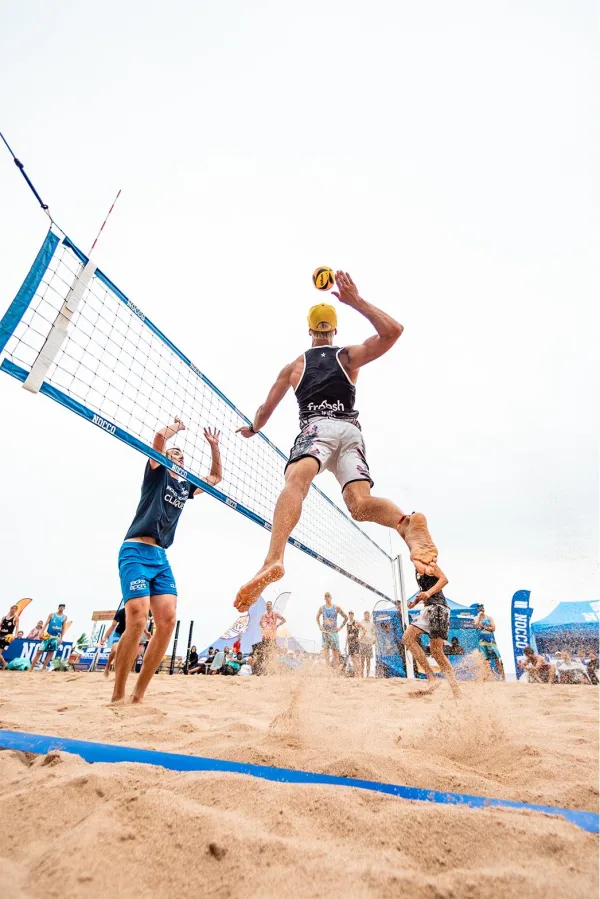 Joueur de beach-volley en plein smash sur terrain de sable