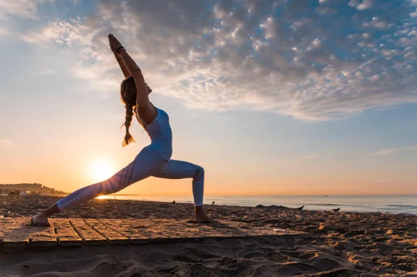 Femme pratiquant le yoga sur la plage au lever du soleil