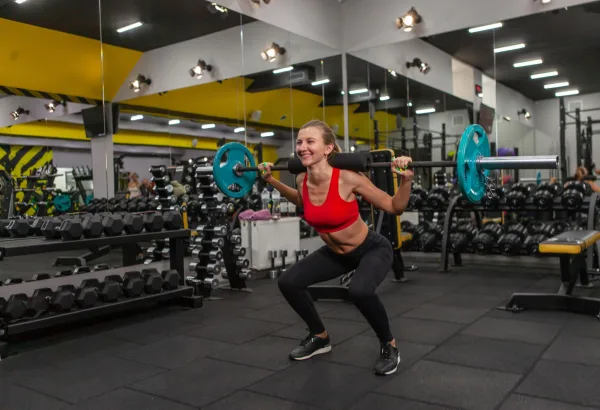 Femme faisant des squats avec une barre en salle de sport