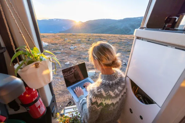 Nomade digitale travaillant depuis un van face à un coucher de soleil en montagne