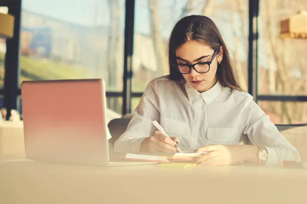 Jeune femme prenant des notes à côté de son ordinateur portable au bureau