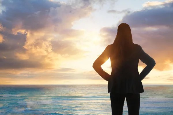 Femme contemplant l'horizon au lever du soleil, symbole de confiance en soi, d'ambition et de nouveaux horizons
