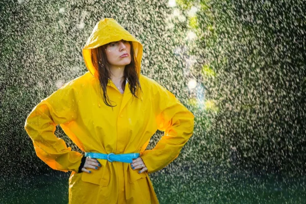 Femme sous la pluie en imperméable jaune, symbole de résilience, de confiance en soi et de force face aux difficultés