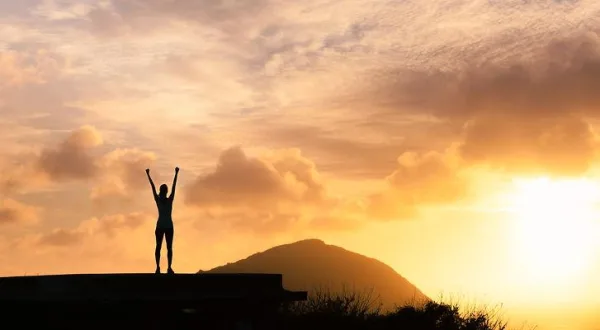 Silhouette célébrant une victoire au lever du soleil, symbole de réussite, de motivation et de dépassement de soi