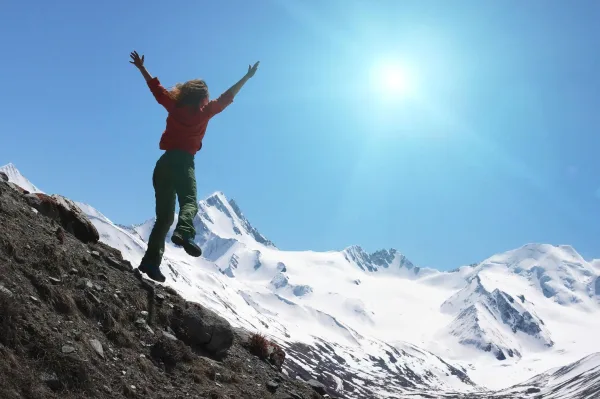 Femme célébrant sa réussite au sommet d'une montagne enneigée sous un ciel bleu