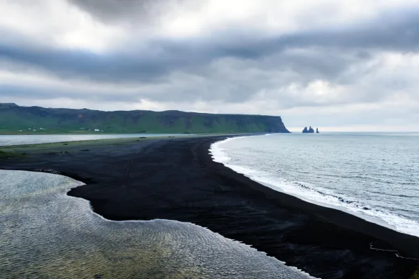 Plage de sable noir sauvage bordée par l'océan sous un ciel nuageux