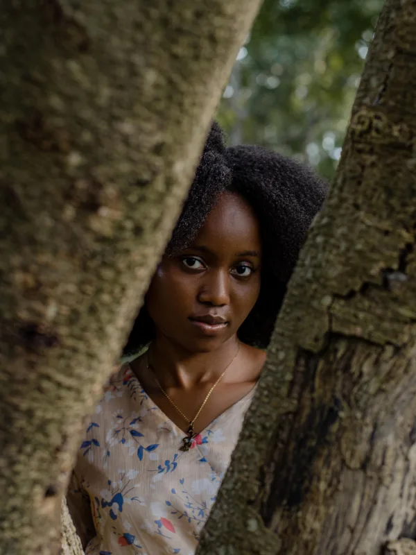 Portrait d'une jeune femme regardant à travers les troncs d'un arbre en forêt
