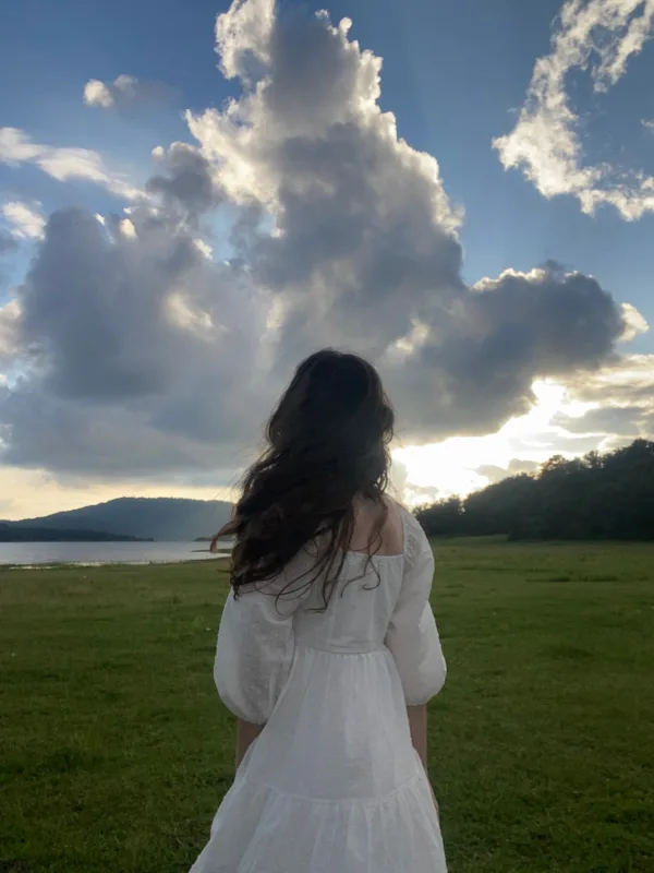 Femme en robe blanche admirant un coucher de soleil sous un ciel spectaculaire au bord d'un lac