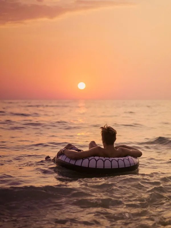 Personne se relaxant sur une bouée au coucher du soleil en pleine mer